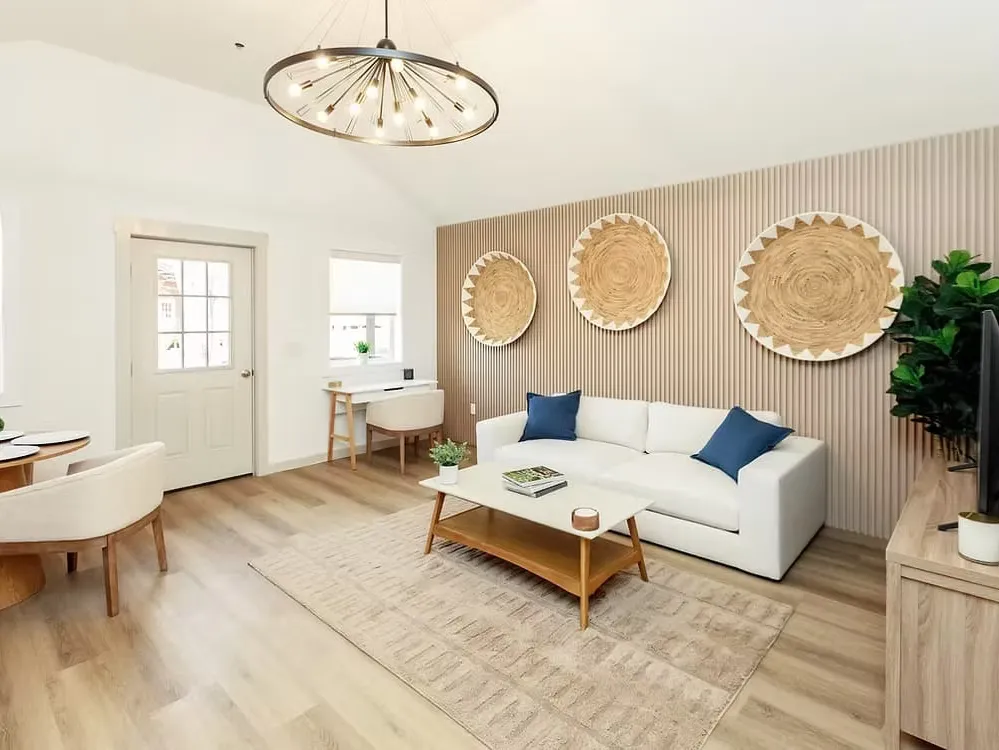 A bright cottage living room with a white sofa, woven wall art and a desk by the door