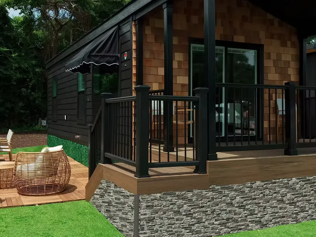 A cottage with cedar-shake siding, a striped awning and a black porch railing