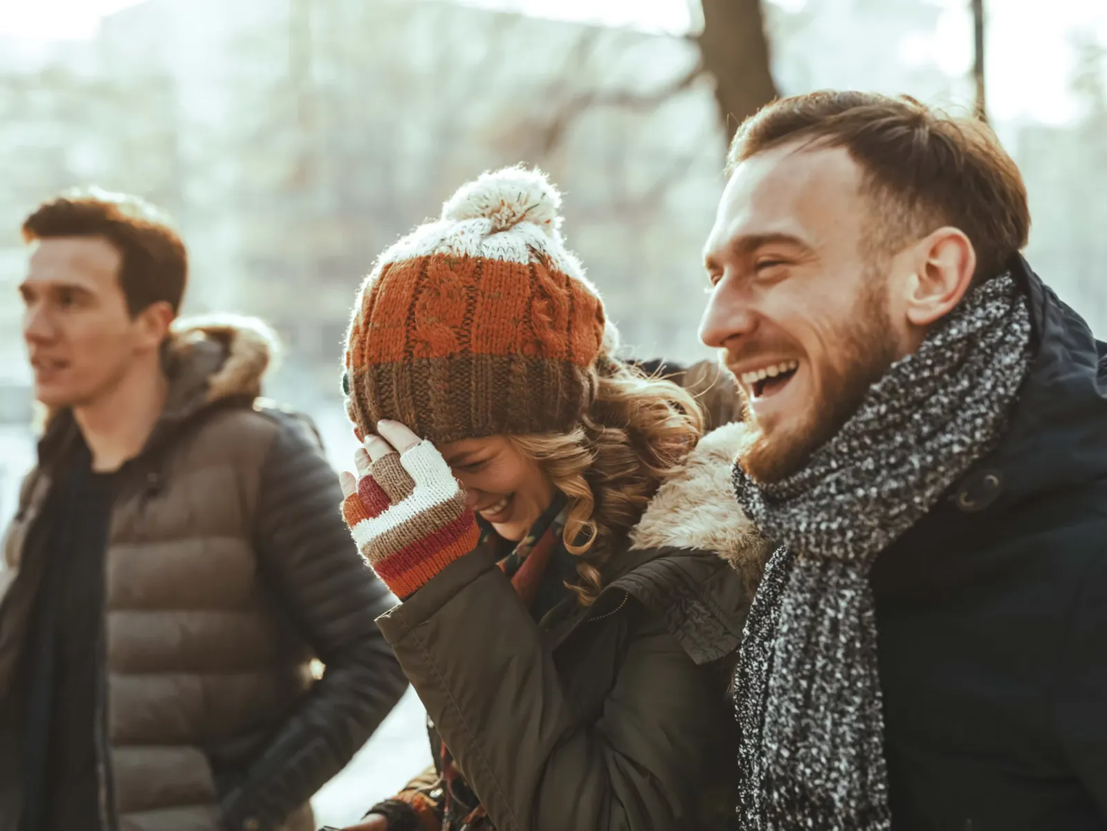 Friends in winter hats and scarves laughing outdoors