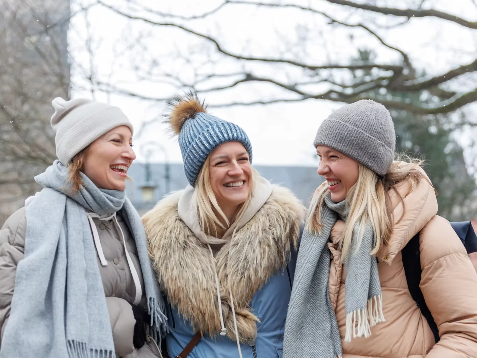 Three friends in winter hats and scarves laughing on a winter day