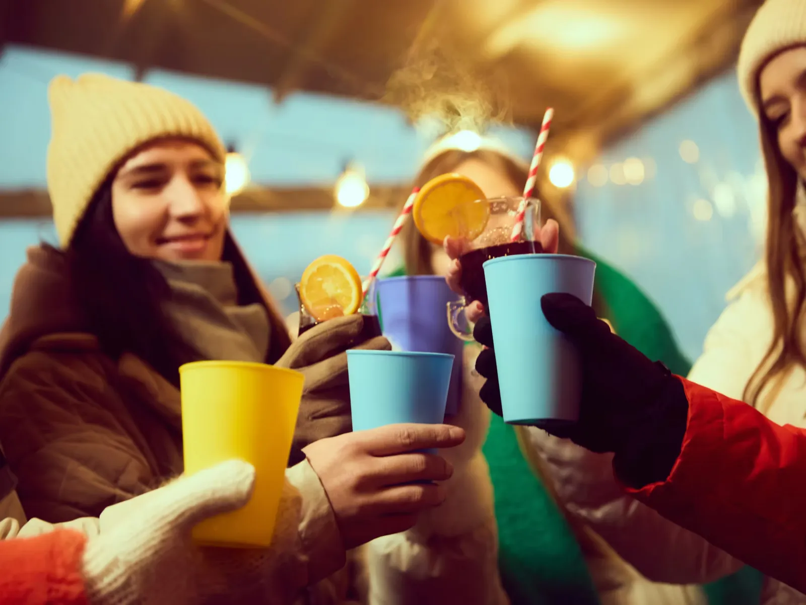 Friends in winter hats raising cups of mulled wine with orange slices