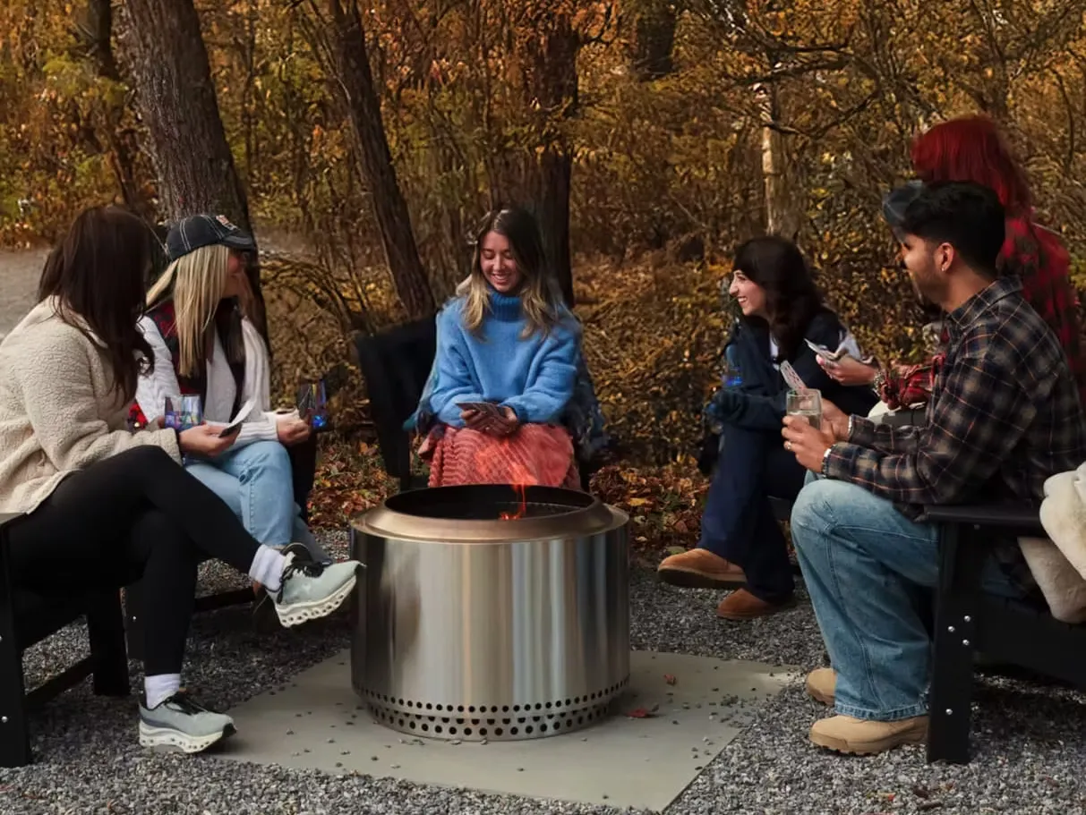 Friends gathered around a Solo Stove among fall trees