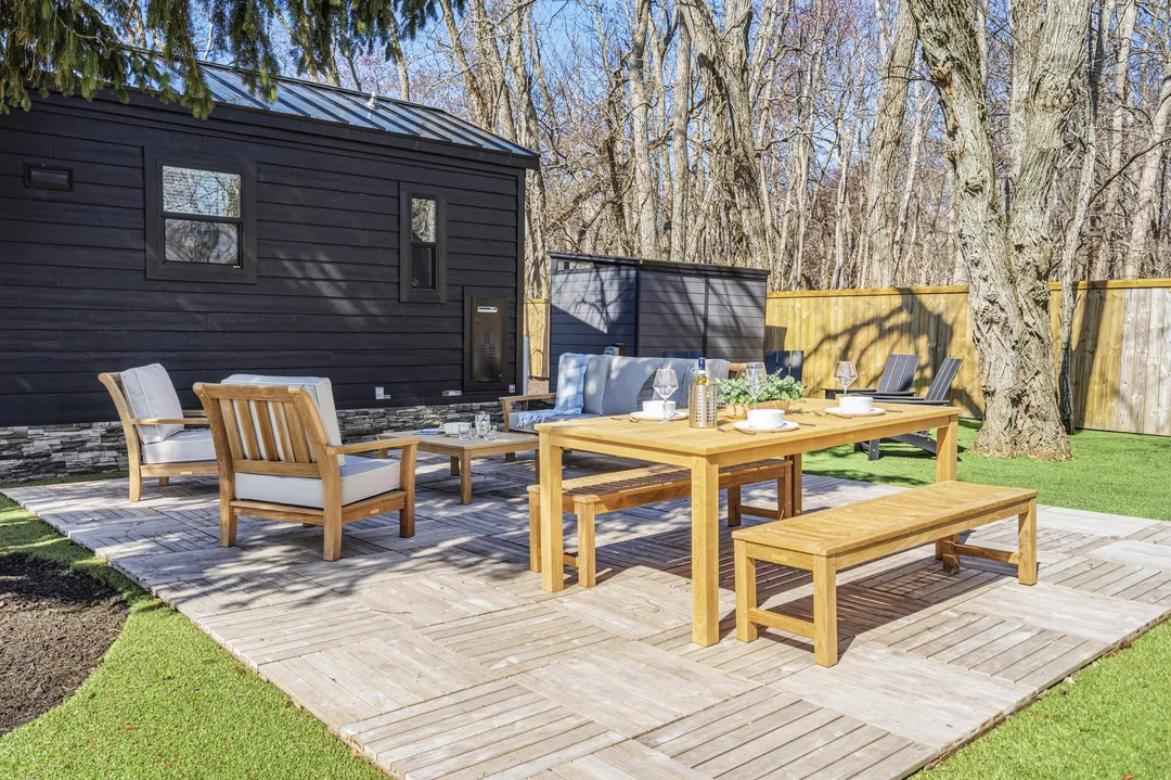 A cottage deck with a wood dining table, benches and lounge chairs