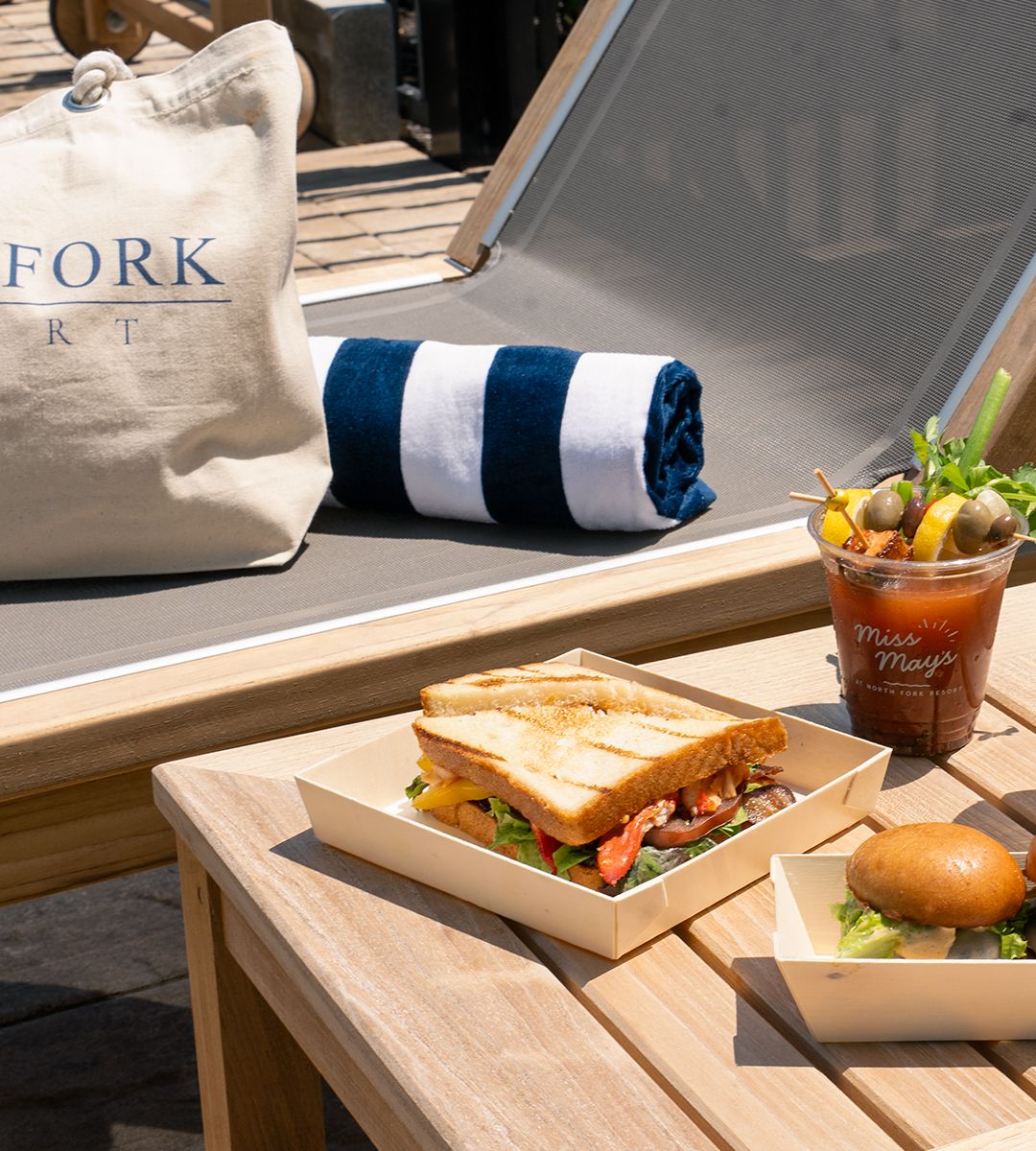 A BLT, a burger slider and a Bloody Mary in a Miss May's cup on a poolside table at North Fork Resort